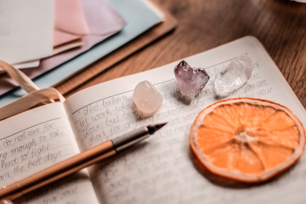 pexels-photo-3363098 Aesthetic journal scene featuring crystals, a pen, and a dried orange slice on a wooden table.