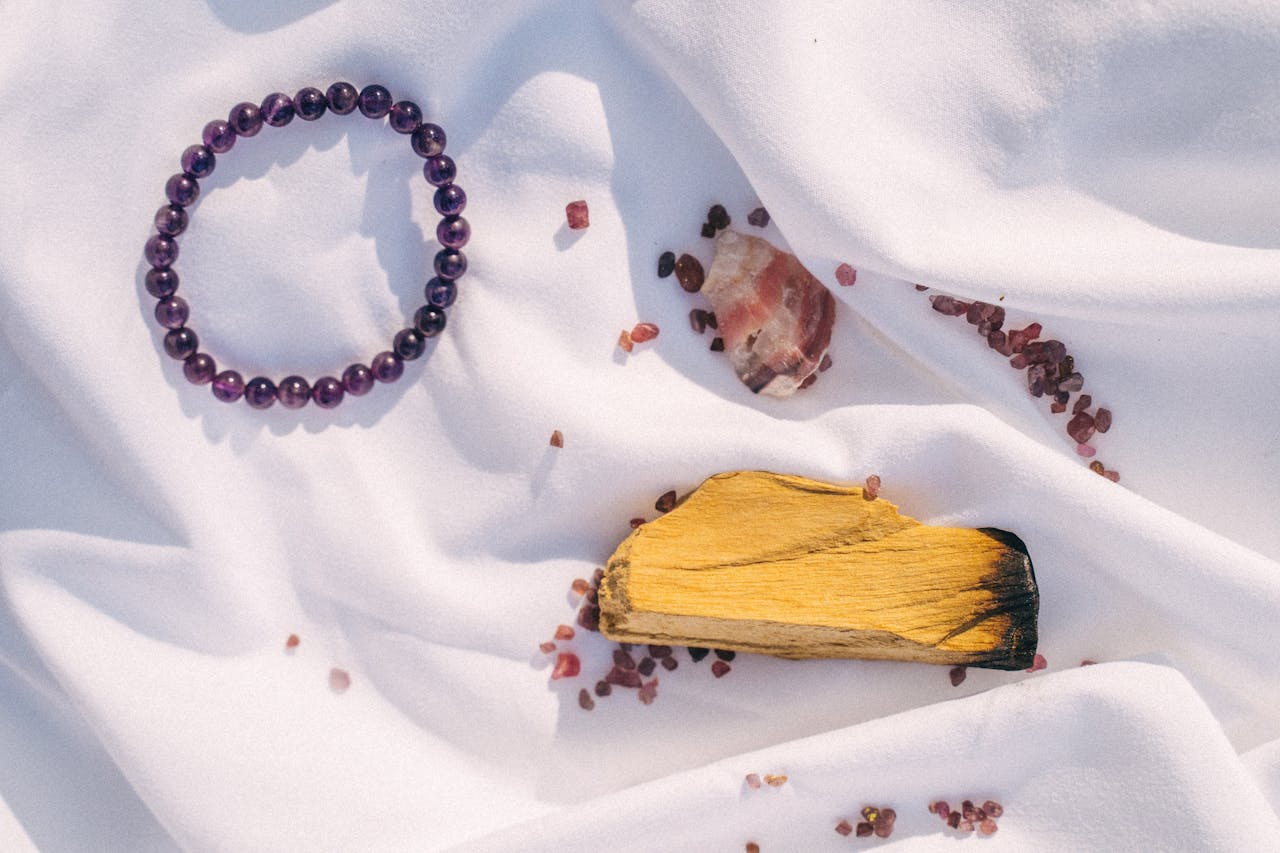 Amethyst bracelet, Palo Santo, and crystals arranged on white fabric for spiritual healing.
