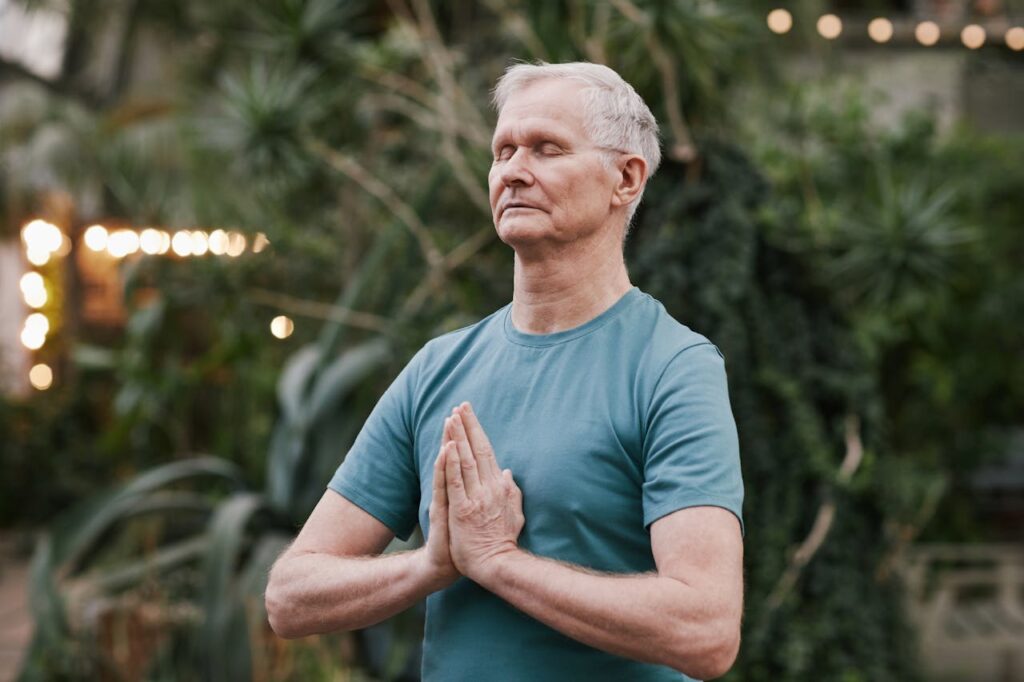 pexels-photo-6787354 Serene elderly man meditating outdoors in a tranquil garden setting, focusing on peace and mindfulness.